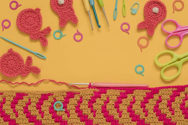 Creative background with crochet fabric, crochet tools and knitted bunnies on a yellow background. Top view. Copy space,