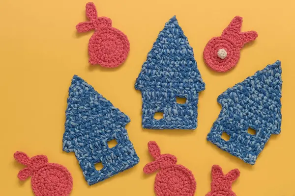 Mini blue crochet houses and Easter bunnies on a yellow background.