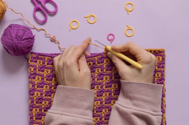 Dişi eller, soyut mozaik desenli parlak kumaş örer. Üst görünüm.