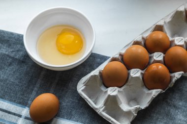 Kırık yumurtalı beyaz bir tabak ve gri bir peçetenin üzerinde kahverengi tavuk yumurtası..