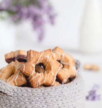 Güneş şeklinde kısa kurabiyeler. Süt şişesi ve leylak kaplamalı bulanık bir arka planda örgü sepetin içinde..