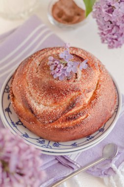 Geleneksel taze tarçınlı çörek, leylak çiçekleriyle dolu bir masaya yakın duruyor. Kanelbullar - İsveç tarçını ruloları.