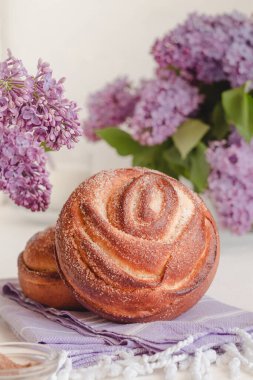 Lezzetli tarçınlı çörek, leylak çiçekleriyle dolu bir masaya yakın duruyor. Kanelbullar - girdaplı tarçın ruloları, girdaplar.