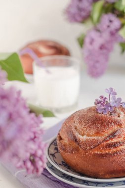 Kanelbullar - İsveç tarçınlı rulo. Süt şişesi ve leylak çiçekli taze pişmiş tarçınlı çörekler. Yan görünüm.