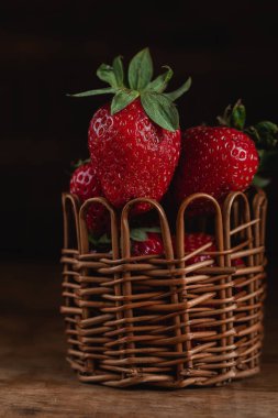 Kahverengi sepetin içinde koyu kırsal bir zeminde taze kırmızı çilekler..