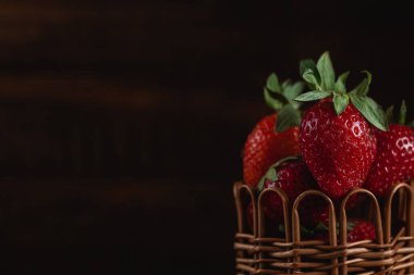 Taze kırmızı çilekler sepetin içinde, siyah tahta bir masanın üzerinde. Taze organik kırmızı meyveler.