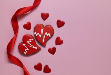 Red heart shaped gingerbread and red satin ribbon on a pink background. Love concept. Copy space.