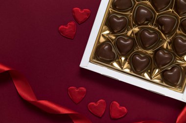 Gift box with heart shaped chocolate candies on a burgundy background. Valentine's day concept. Top view. Copy space.