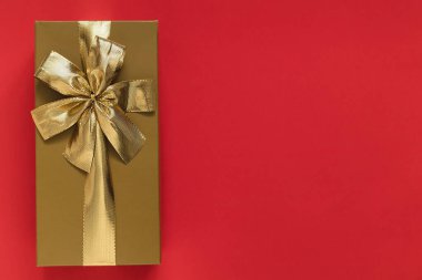 Golden gift box with golden ribbon and bow on a red background. Top view. Copy space.