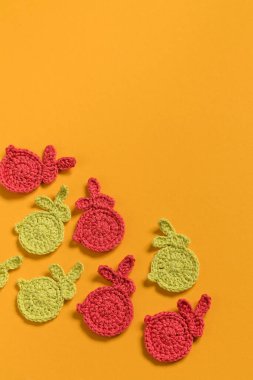 Cute handmade Easter decor on a yellow background. Small red yellow crochet bunnies. Top view. Copy space.