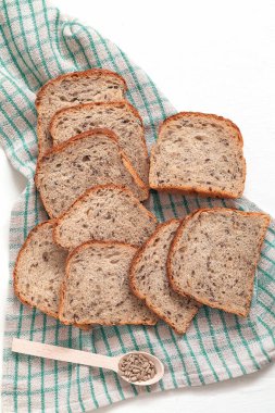 Taze tahıllı ekmek, ay çekirdeği ve keten peçeteye keten serpiştirilmiş beyaz arka plan. Sağlıklı fırın ürünü.