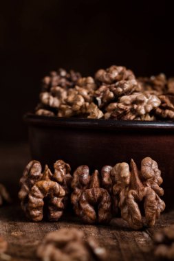 Koyu ahşap bir masada seramik kasenin yanındaki organik ceviz çekirdekleri. Ceviz çekirdekleri kapanır.