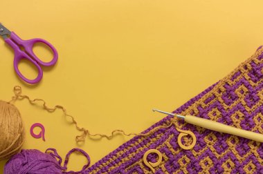 Soyut desenli tığ işi kumaş, tığ işi kanca, makas, sarı arka planda örgü kalemleri ve iplikler. Boşluğu kopyala.