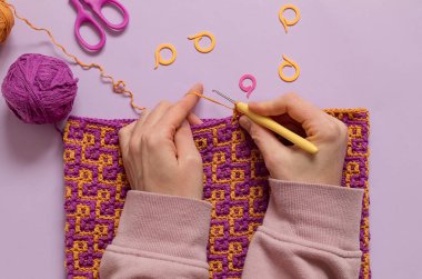 Dişi eller, soyut mozaik desenli parlak kumaş örer. Üst görünüm.