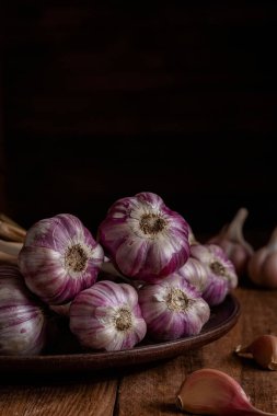 Kahverengi seramik tabakta ahşap bir zeminde taze mor sarımsak. Boşluğu kopyala.