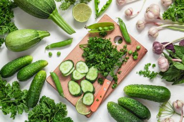 Taze sebzeler ve beyaz arka planda kesim tahtası. Salatalık, sarımsak, bezelye, maydanoz, fesleğen, kabak. Taze yeşil ürün. Üst görünüm.
