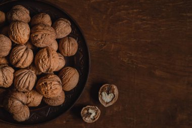 Ahşap bir arka planda koyu bir tabakta soyulmamış kahverengi ceviz. Boşluğu kopyala.