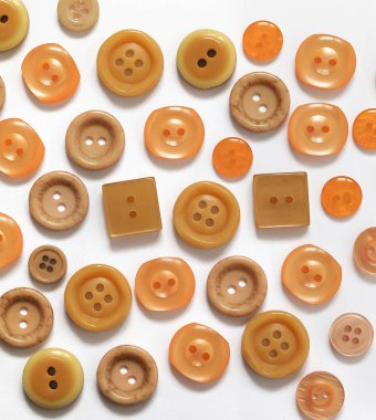 Beyaz zemin üzerinde farklı boyutlarda ve şekillerde bej ve mercan plastik düğmeler koleksiyonu.