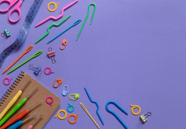 Mor bir arka planda örülmüş ve tığ işi aletlerle dolu bir defter. Üst Manzara. Boşluğu kopyala.