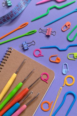 Not defteri, mor bir arka planda renkli örgü ve örgü aletleri. Üst görünüm.