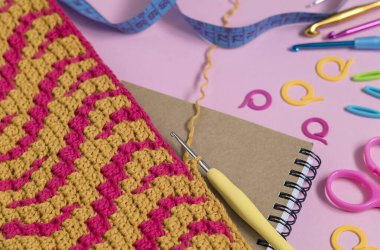 Pembe arka planda tığ işi kumaş ve tığ işi araçları olan çalışma alanı.