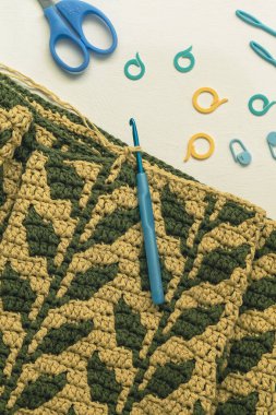 Yapraklarla sıcak bir battaniye örme süreci. Sarı yeşil tığ işi kumaş ve tığ işi aletleri.