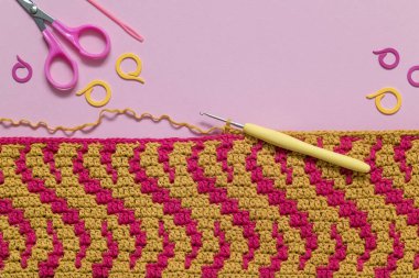 Pembe arka planda Magenta sarı örgü örme kumaşı ve tığ işi aletleri. Üst Manzara. Boşluğu kopyala.