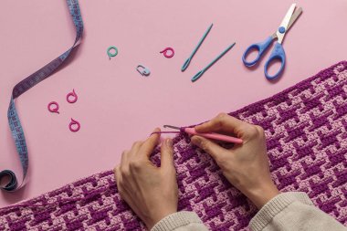Mor mozaik battaniye ören kadın elleri. Pembe arka planda tığ işi kumaş ve tığ işi aletleri. Üst Manzara. Boşluğu kopyala.