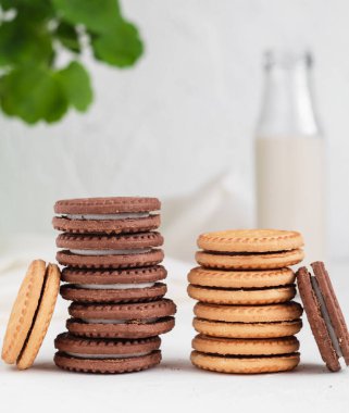 İki yığın kahverengi ve altın kurabiyeyle beyaz bir masada krema ve süt..