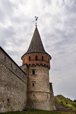 Ortaçağ kalesinin kulesinde dayanıklı taş duvarlar ve yemyeşil ve karamsar bulutların zeminine kurulmuş kendine özgü konik bir çatı bulunur.