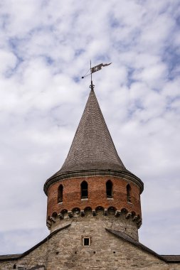 Bir ortaçağ kalesinin kulesi, tarihi önemi ve mimari güzelliği vurgulayan dramatik bir gökyüzü ile çevrili konik bir çatı ve karmaşık taş işçiliğine sahiptir.