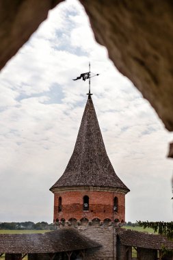 Ortaçağ kalesinin kulesinde antik taş duvarlar ve canlı yeşilliklerle çerçevelenmiş eşsiz bir kule ve rüzgar gülü bulunur.