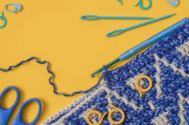 Örgü kancalı mavi beyaz örgü kumaş, makas ve sarı arka planda örme işaretleri. Üst Manzara. Boşluğu kopyala.
