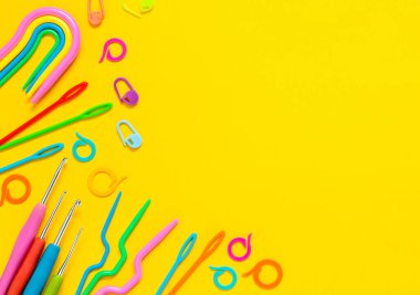 Sarı arka planda örgü aletleri. Tığ işi kancalar, plastik örgü iğneleri, işaretleyiciler, eğri iğneler. Düz yatıyordu. Boşluğu kopyala.