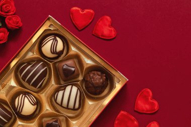 Gift box with chocolate candies and red heart decoration for Valentine's Day on a burgundy background. Top view. Copy space.