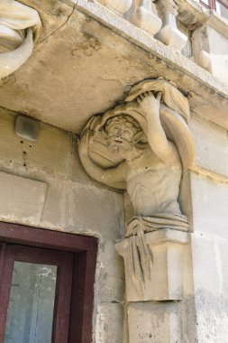 Taş heykelde, büyük bir sarayda sanatsal ayrıntıları ve tarihi mimariyi vurgulayan ağır bir yük taşıyan bir figür yer alıyor.