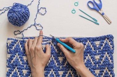 Kadın elleri, tığ işi kancayı ve soyut mozaik desenli mavi beyaz ctochet kumaşı tutuyor. Üst Manzara. Boşluğu kopyala.