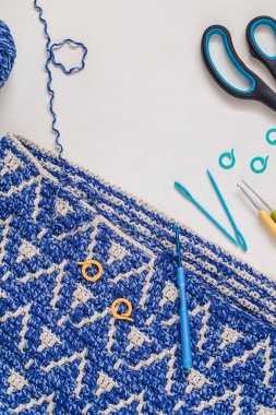 Beyaz arka planda soyut mavi örgü kumaş ve tığ işi aletler. Üst Manzara. Boşluğu kopyala.