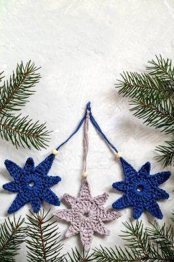 El yapımı örgü dekoru. Beyaz arka planda gri, mavi, tığ işi yıldız şekilli Noel ağacı oyuncakları ve köknar dalları. Boşluğu kopyala.