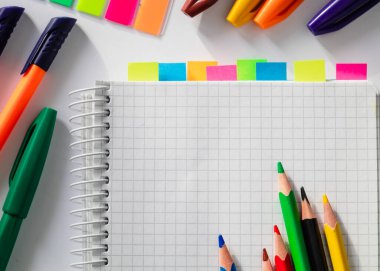 Üzerinde renkli çıkartmalar ve beyaz arka planda renkli kalemler olan beyaz boş kağıtlı defteri aç. Boşluğu kopyala.