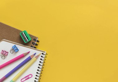 Sarı arka planda okul malzemeleri. Defterler, kalemler, kalemler. Üst Manzara. Boşluğu kopyala.