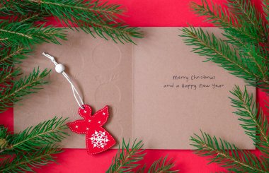 Noel arkaplanı tebrik kartı, kırmızı tahta melek ve köknar ağacı dalları. Kırmızı arka planda Noel kompozisyonu. Üst Manzara. Boşluğu kopyala.