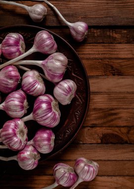 Kırsal ahşap arka planda kahverengi bir tabakta taze mor sarımsak soğanları. Üst görünüm.