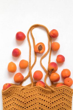 Beyaz arka planda taze organik kayısılarla örgü örülü sarı alışveriş torbası. Sağlıklı beslenme konsepti. Üst Manzara. Boşluğu kopyala.