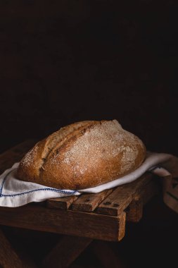 Koyu arkaplanda beyaz keten peçetede taze pişmiş çavdar ekmeği..