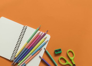 Not defteri ve turuncu arka planda parlak pastel kalemler. Üst Manzara. Boşluğu kopyala.