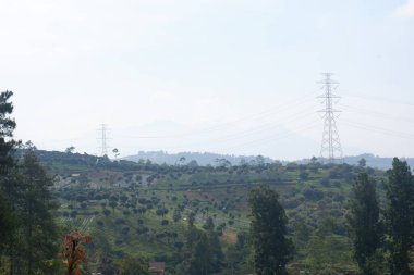 Yüksek voltaj direklerinin bulunduğu tepenin manzarası bulutlu bir gökyüzünün altında duruyor, elektrik iletimi.