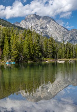 Grand Tetons 'un yüksek dağlarının altında kano küreklerinin keyfini çıkaran birkaç insanın güzel ve yansıtıcı bir görüntüsü..