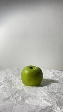 Yeşil elma tabakta hala hayat fotoğrafı, buruşmuş kağıt, beyaz arka planda sert beyaz ışıklandırmalı toprak