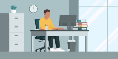 Yaratıcı genç bir çalışan ofis masasında oturuyor ve bilgisayarla çalışıyor.